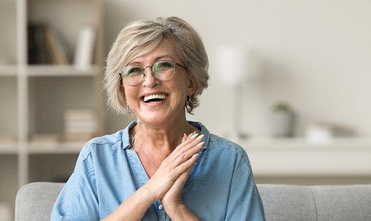 Senior woman with glasses smiling on couch at home