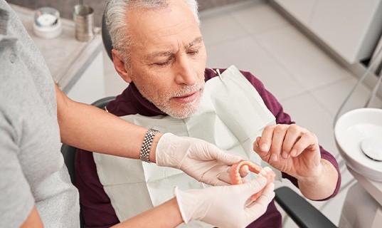 Gloved hands handing new dentures to man in dental chair