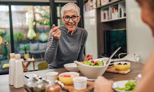 Woman with black glasses smiling while eating with friend