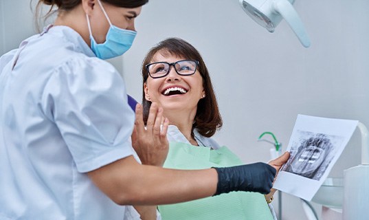 Woman smiling with dentist while reviewing X-ray