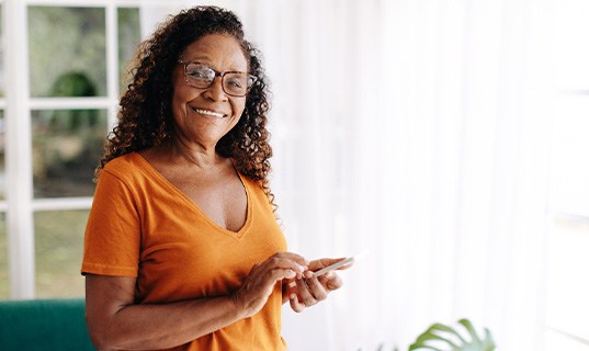 Senior woman with glasses smiling while looking at phone