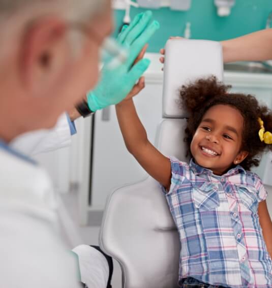 Smiling child giving children's dentist high five during dental checkup and teeth cleaning visit