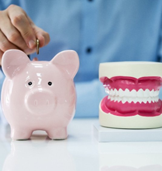 A man putting a coin in a piggy bank that’s sitting next to a model jaw