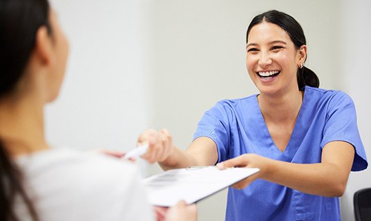 Dentist in white gloves holding model tooth in one hand and making “ok” sign with other