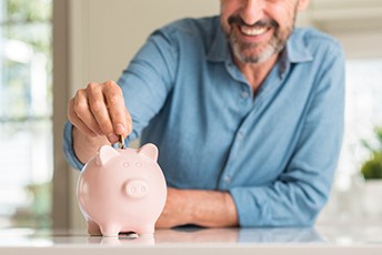 Smiling man placing coins in a piggy bank