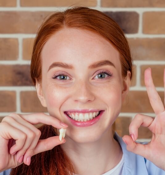 Smiling woman holding an extracted wisdom tooth